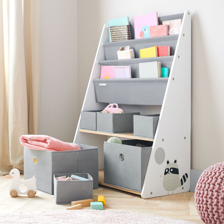 En un apartamento hay un estante organizador Racoon de la marca Kinderkraft. Dentro de sus compartimentos hay contenedores llenos de juguetes y libros.