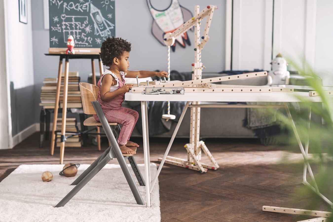 Un niño pequeño de pelo negro construye una estructura de madera, está muy concentrado, está sentado en la silla LIVY Kinderkraft