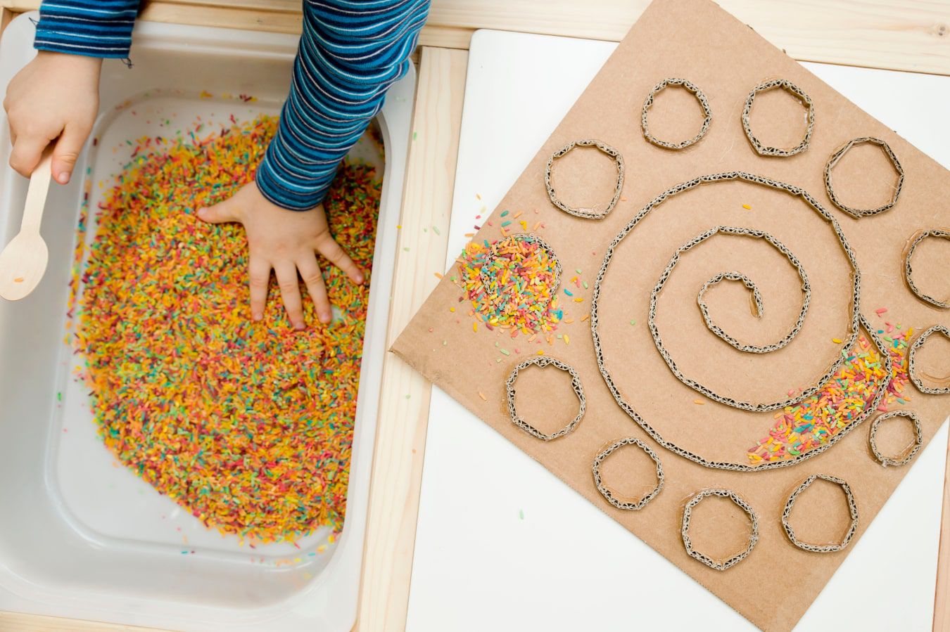 Las manos del niño conocen una textura nueva: caramelos de colores y virutas de chocolate, al lado hay un laberinto de cartón hecho en casa