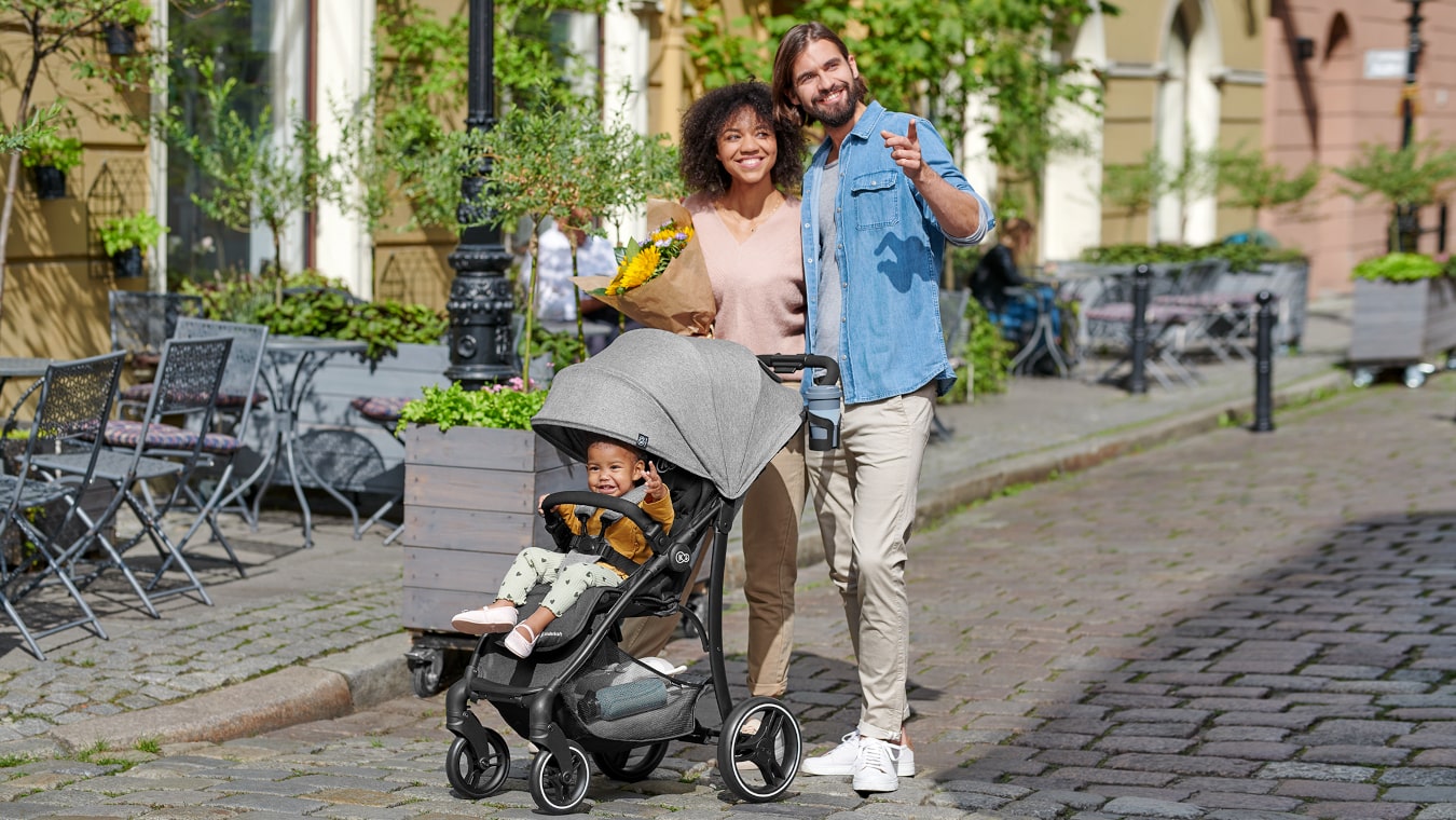 La mamá, el papá y la niña pequeña en la silla de paseo trig de color gris, están dando un paseo por la ciudad.